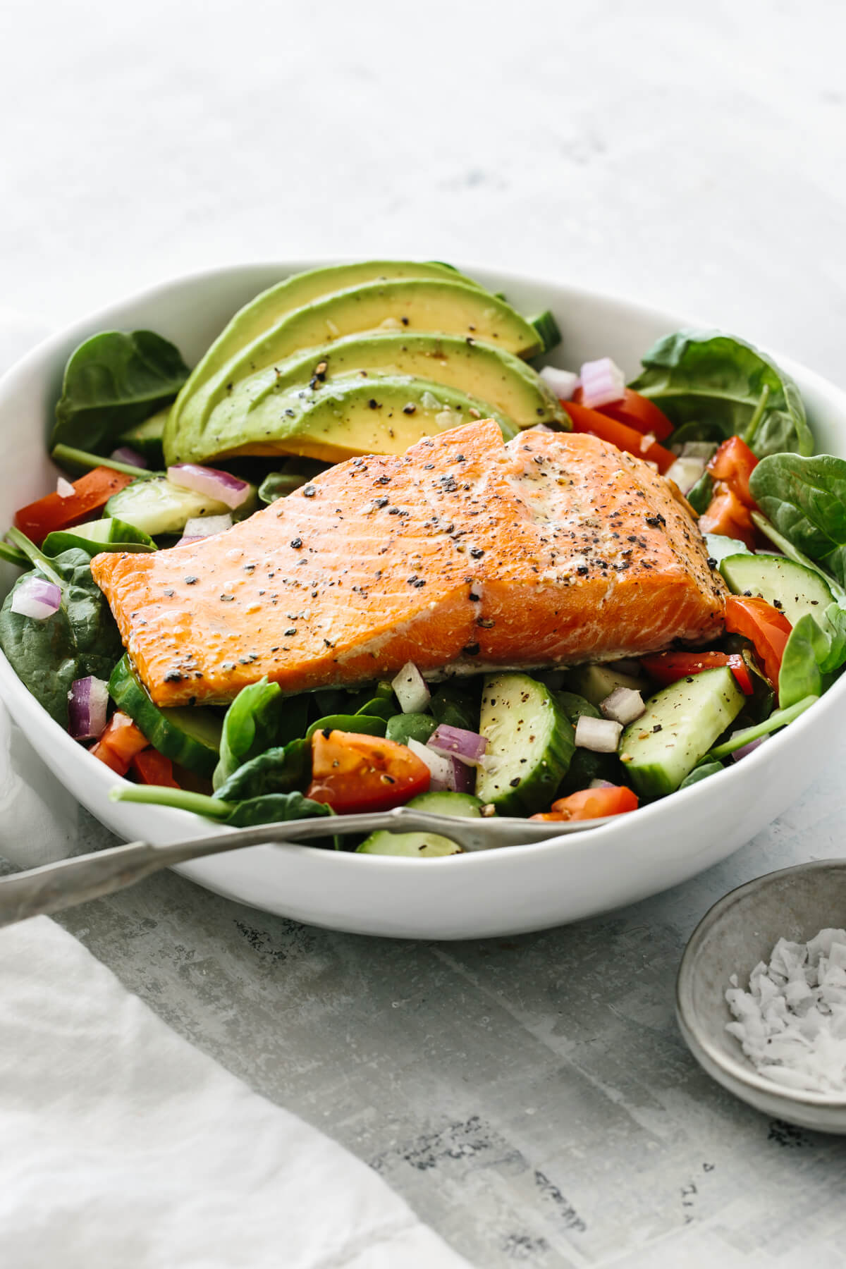 Salmon placed on top of salad recipe with avocado and other ingredients.