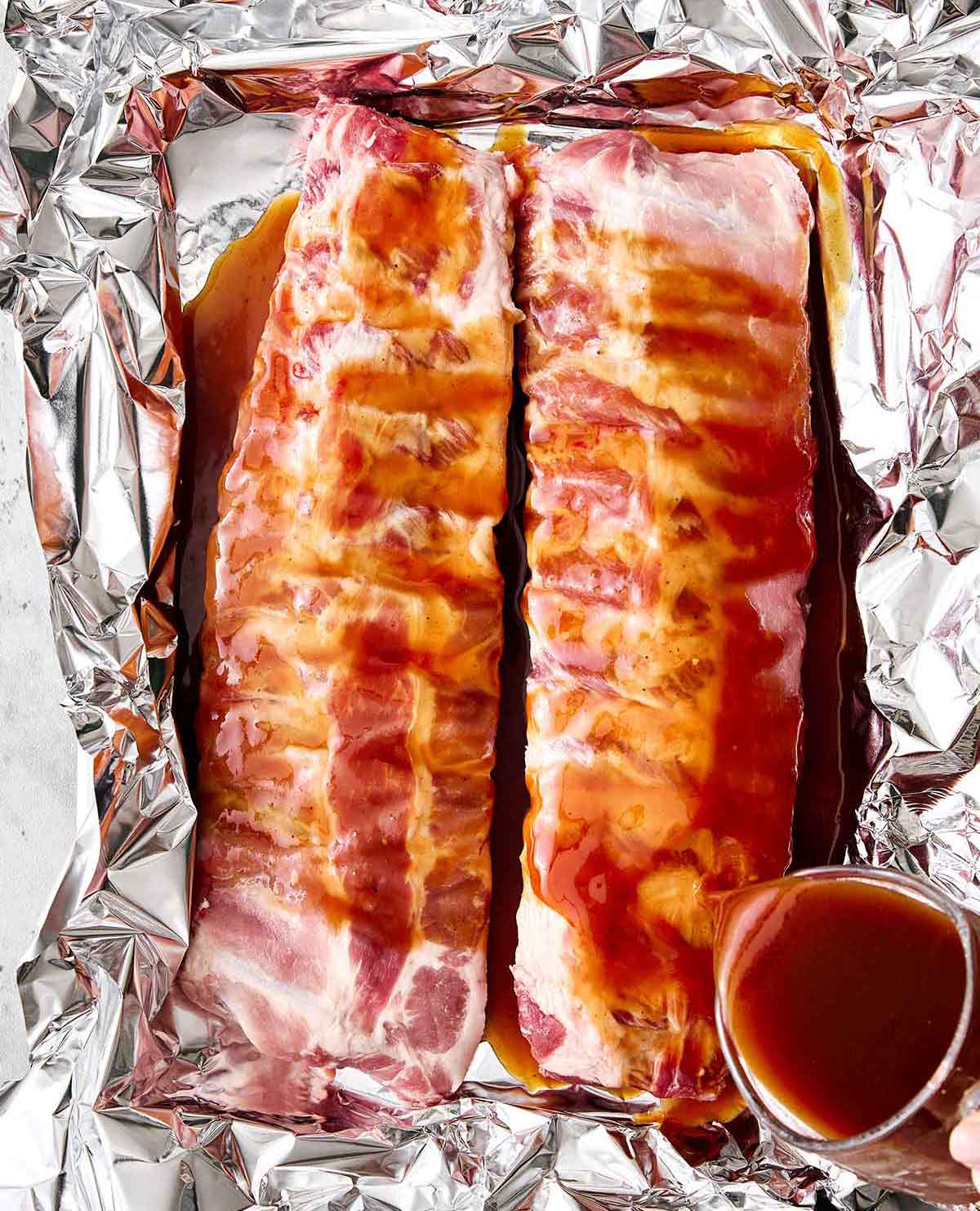 These baby back ribs are my secret to the best cookout meal. Guaranteed to be fall-apart tender with the best pineapple BBQ sauce! Pouring sauce over baby back ribs.