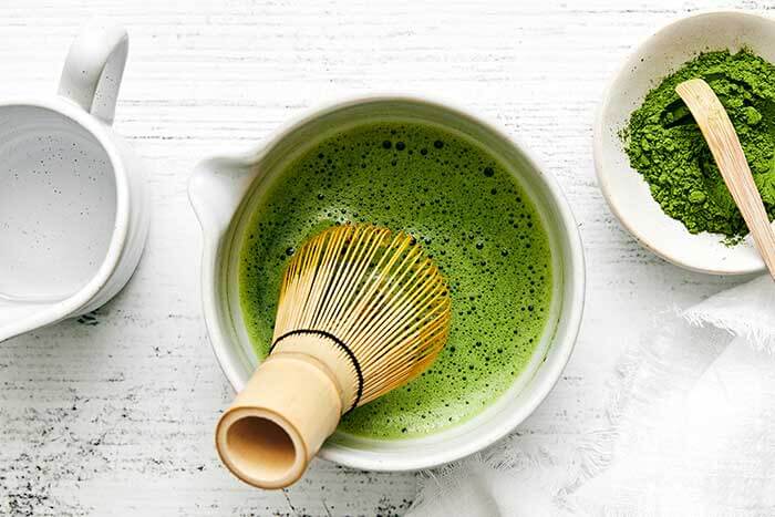 Matcha in a cup with a whisk.