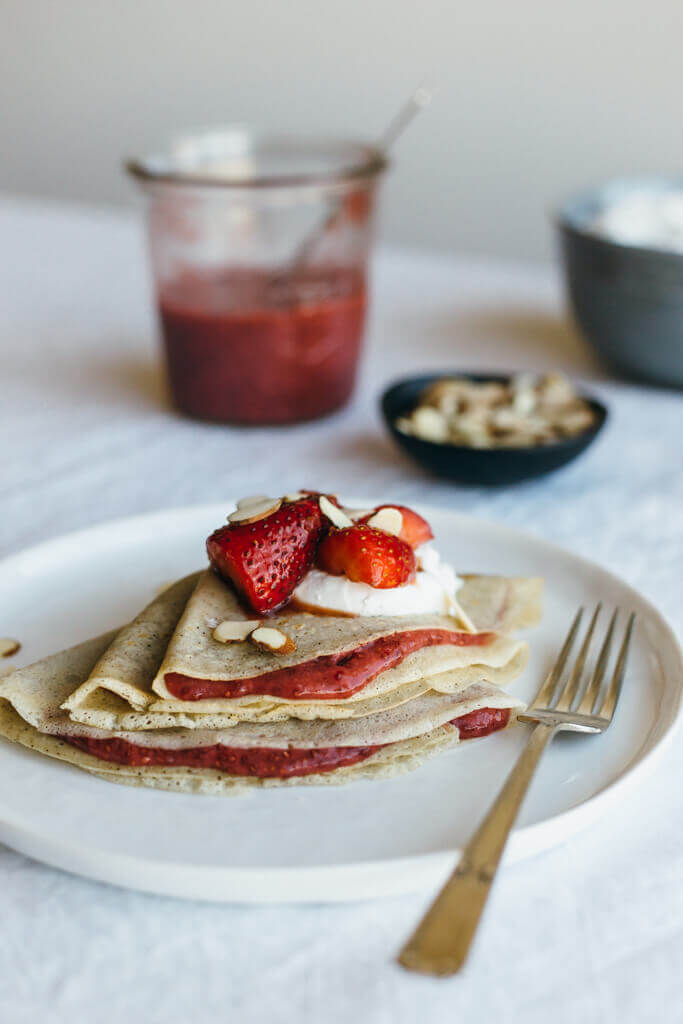 (gluten-free, paleo) Vanilla bean cassava flour crepes with strawberry chia jam. Sweet breakfast crepes are filled with homemade strawberry chia jam and topped with coconut whipped cream and almonds.
