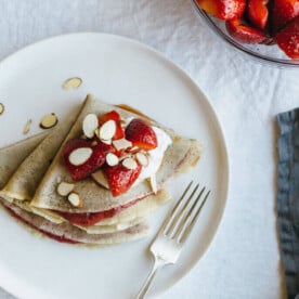 (gluten-free, paleo) Vanilla bean cassava flour crepes with strawberry chia jam. Sweet breakfast crepes are filled with homemade strawberry chia jam and topped with coconut whipped cream and almonds.