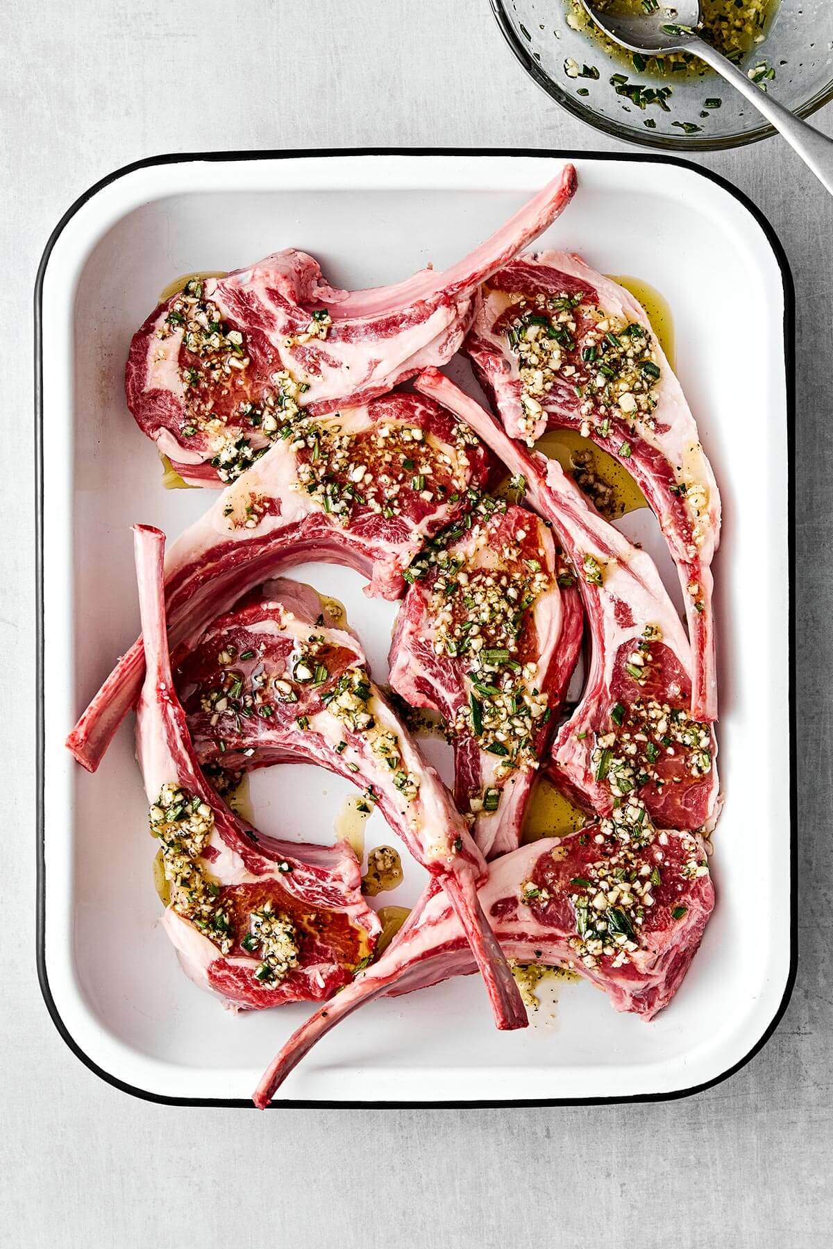 A tray of marinated lamb chops filled with garlic and rosemary.