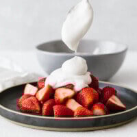 Coconut whipped cream dolloped on a plate of strawberries.