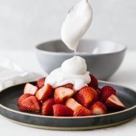 Coconut whipped cream dolloped on a plate of strawberries.