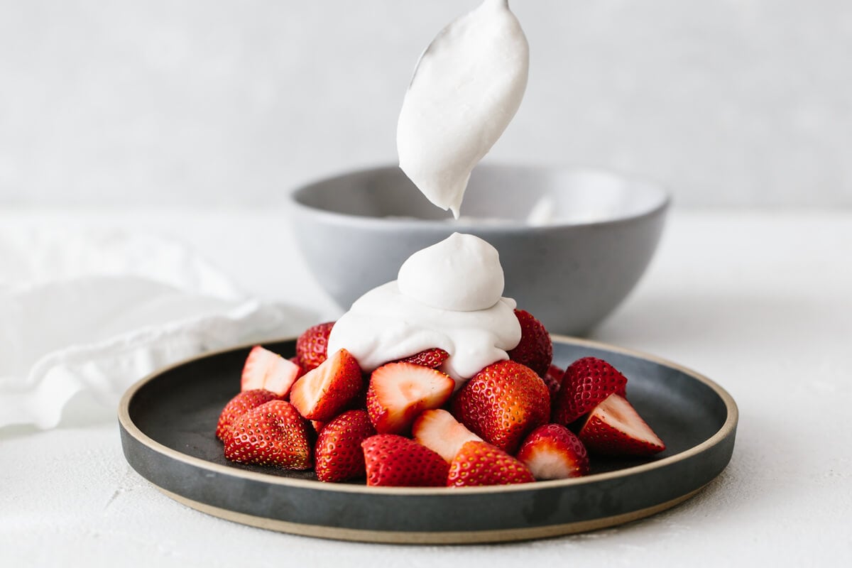 Coconut whipped cream dolloped on a plate of strawberries.