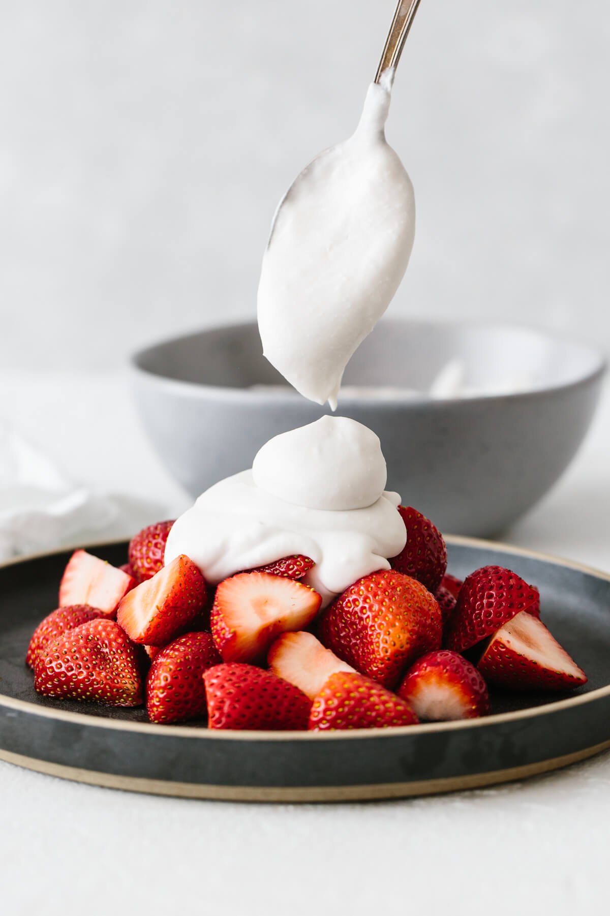 Coconut whipped cream dolloped on a plate of strawberries.