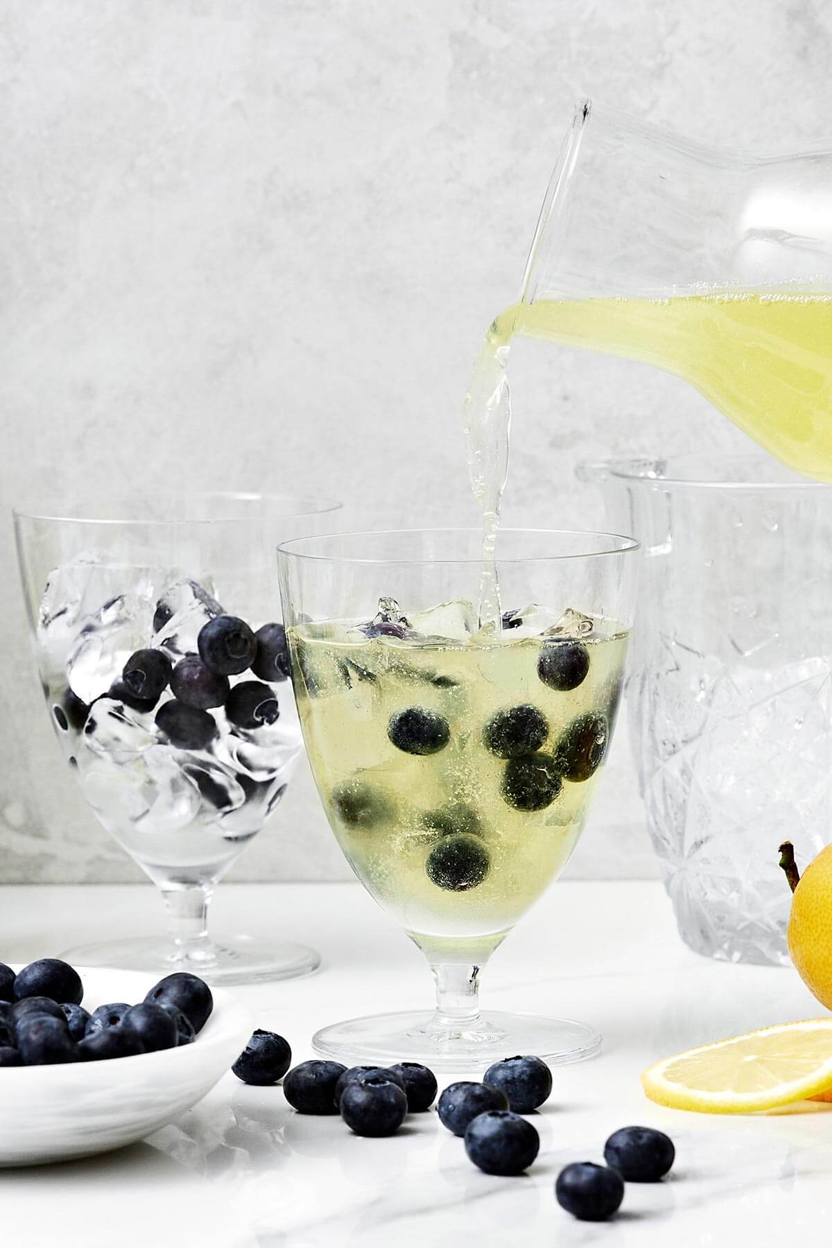 This limoncello prosecco is the summer cocktail you'll be sipping on all season long. It's got sparkling lemony goodness with fresh blueberries and thyme. Pouring limoncello prosecco into a glass.