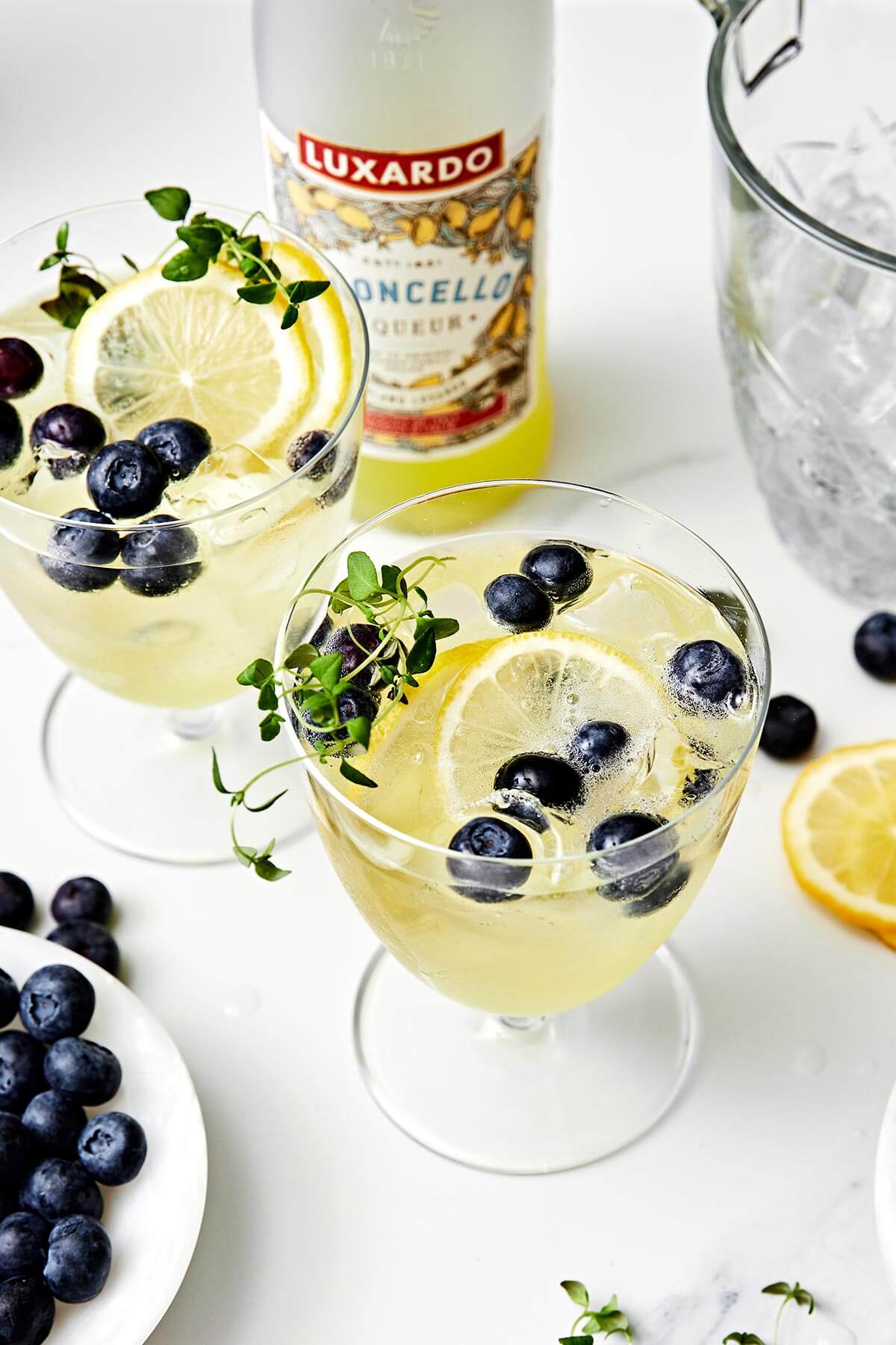 This limoncello prosecco is the summer cocktail you'll be sipping on all season long. It's got sparkling lemony goodness with fresh blueberries and thyme. Glasses of limoncello prosecco.