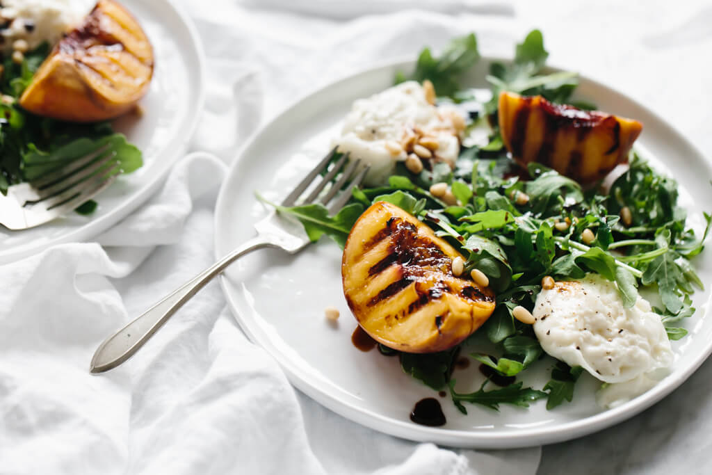 This grilled peach and burrata salad is summertime on a plate. The mix of grilled peaches, arugula, burrata, pine nuts and balsamic is the perfect summer salad recipe. 