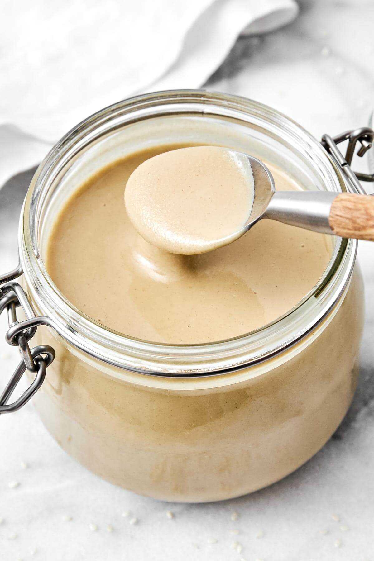 It’s super easy to make homemade tahini in a blender! All you need are sesame seeds and olive oil for a fresh, creamy, and smooth texture. Tahini in a glass jar.
