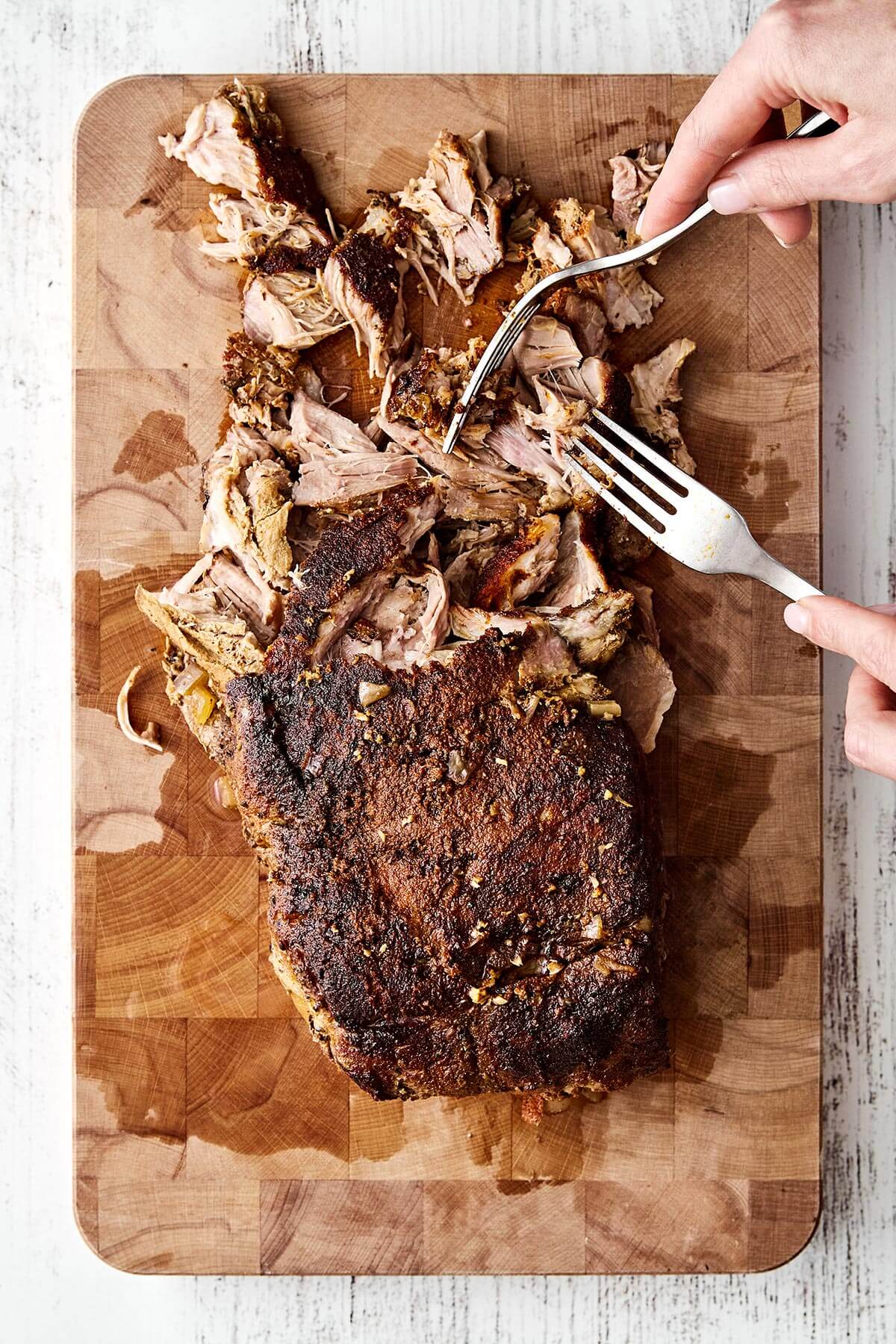 This slow cooker pulled pork is the ultimate “set it and forget” dinner that turns out fall-apart tender and incredibly flavorful every time! Shredding pulled pork on a board.