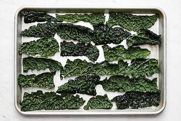 A baking sheet with uncooked kale leaves.