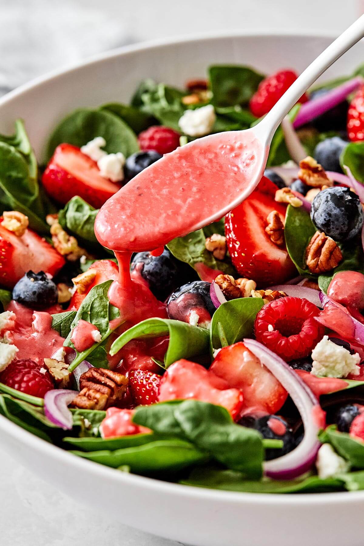 Drizzling raspberry vinaigrette over a berry spinach salad.