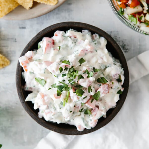 Creamy pico de gallo dip in a black bowl next to chips and salsa.