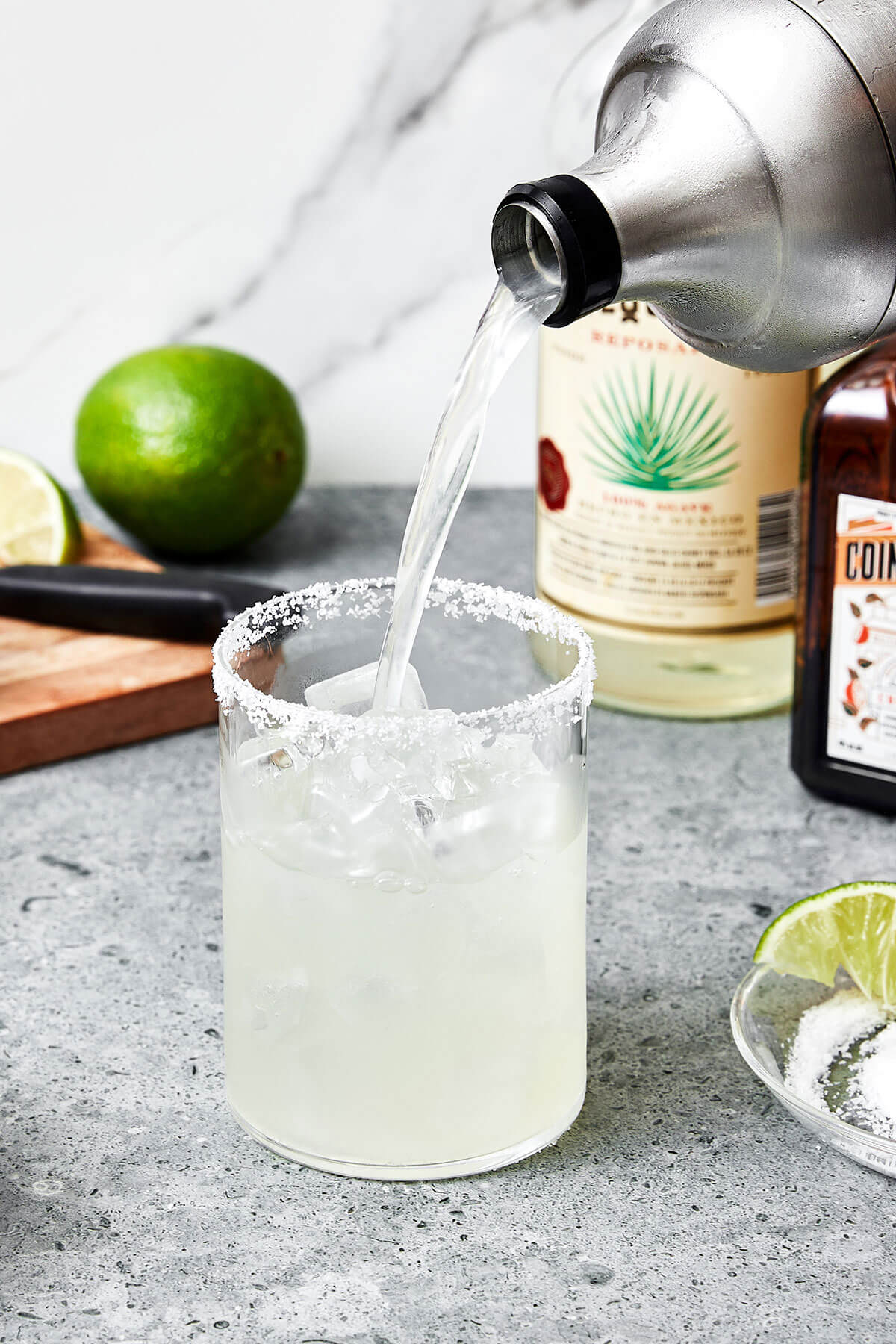 This classic margarita recipe is an easy cocktail with tequila, triple sec, and lime juice. Perfect for serving a crowd! Pouring margarita into a glass.