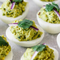 Several avocado guacamole deviled eggs on a white plate.