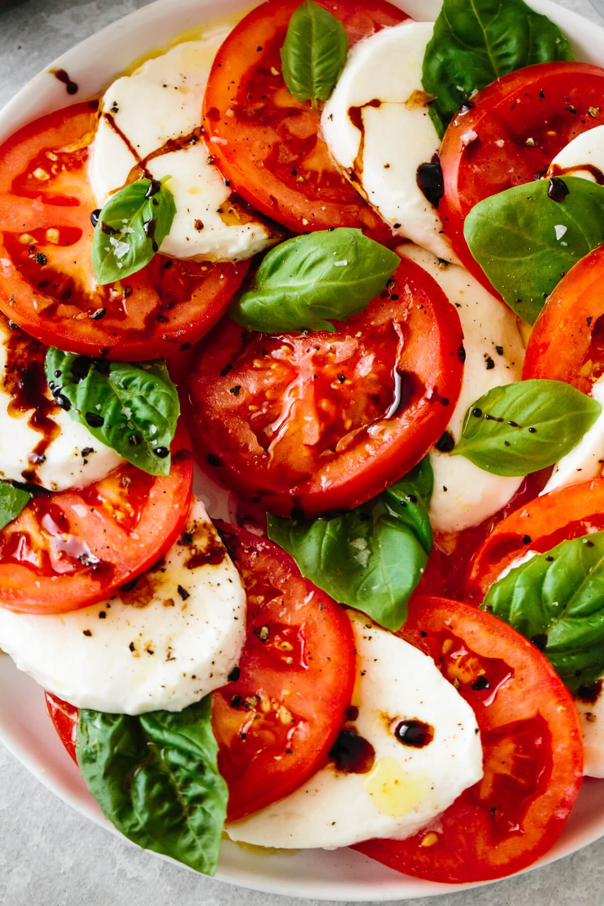 Caprese salad is a classic Italian salad with juicy tomatoes, mozzarella, basil leaves, and drizzled with olive oil and balsamic vinegar. Close up of a caprese salad