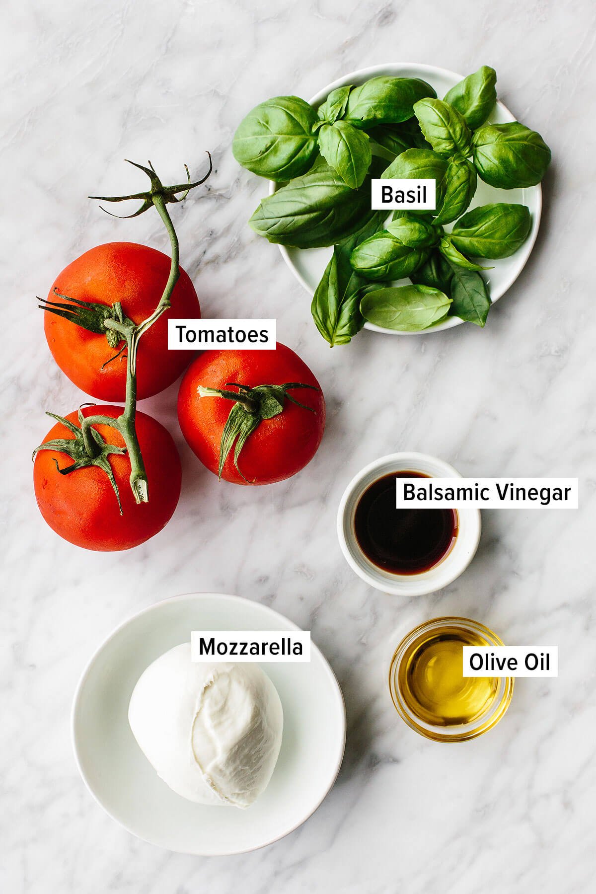 Caprese salad is a classic Italian salad with juicy tomatoes, mozzarella, basil leaves, and drizzled with olive oil and balsamic vinegar. Ingredients for caprese salad on a table