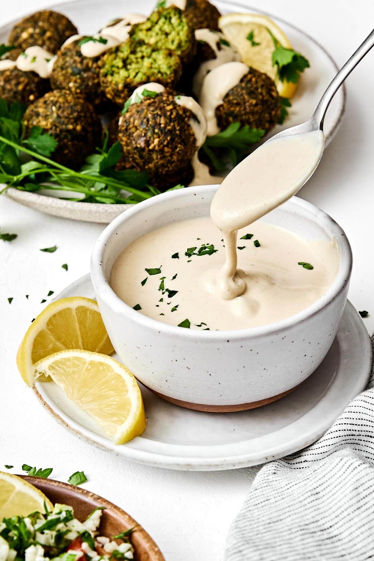 A spoonful of tahini sauce next to falafels.