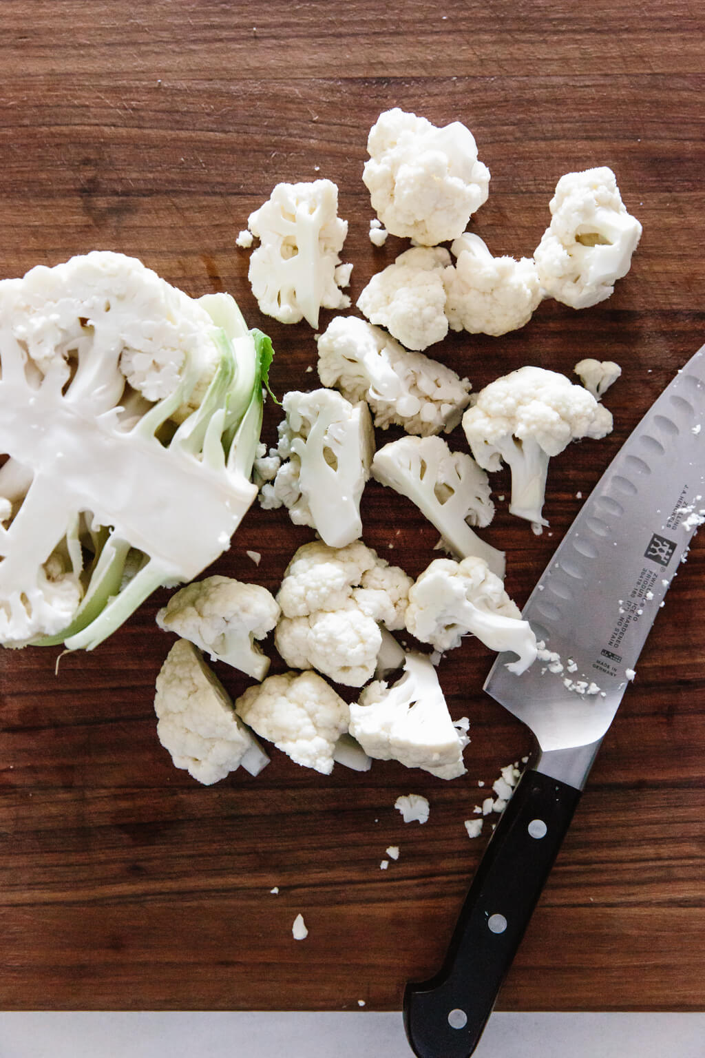 Chopping the florets from a head of cauliflower on a cutting board.