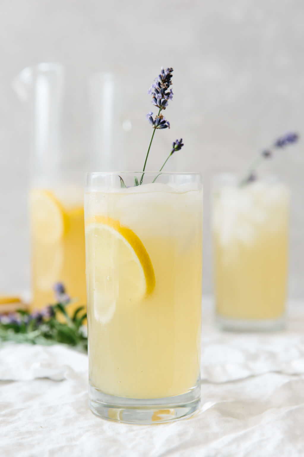 Lavender lemonade in a tall glass with a slice of lemon and sprig of fresh lavender.
