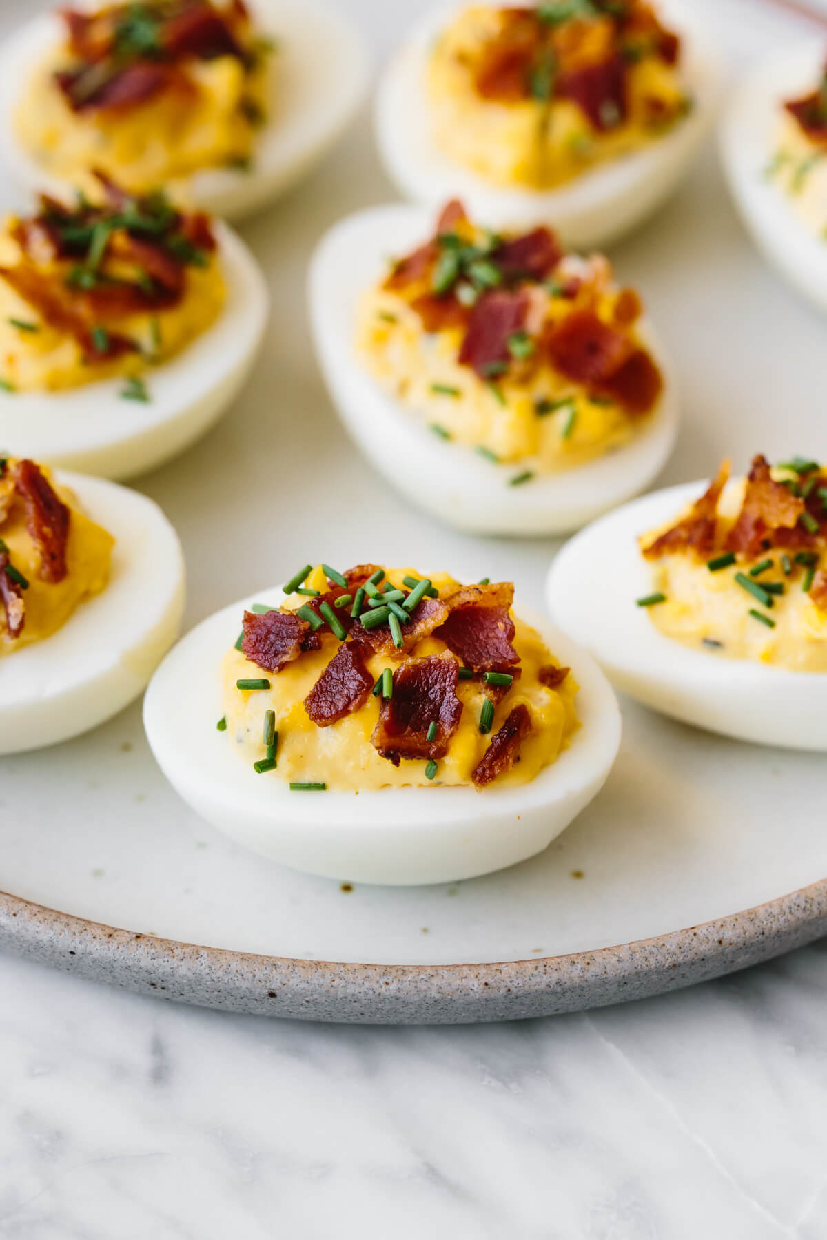 A plate of deviled eggs with bacon and chives sprinkled on top.