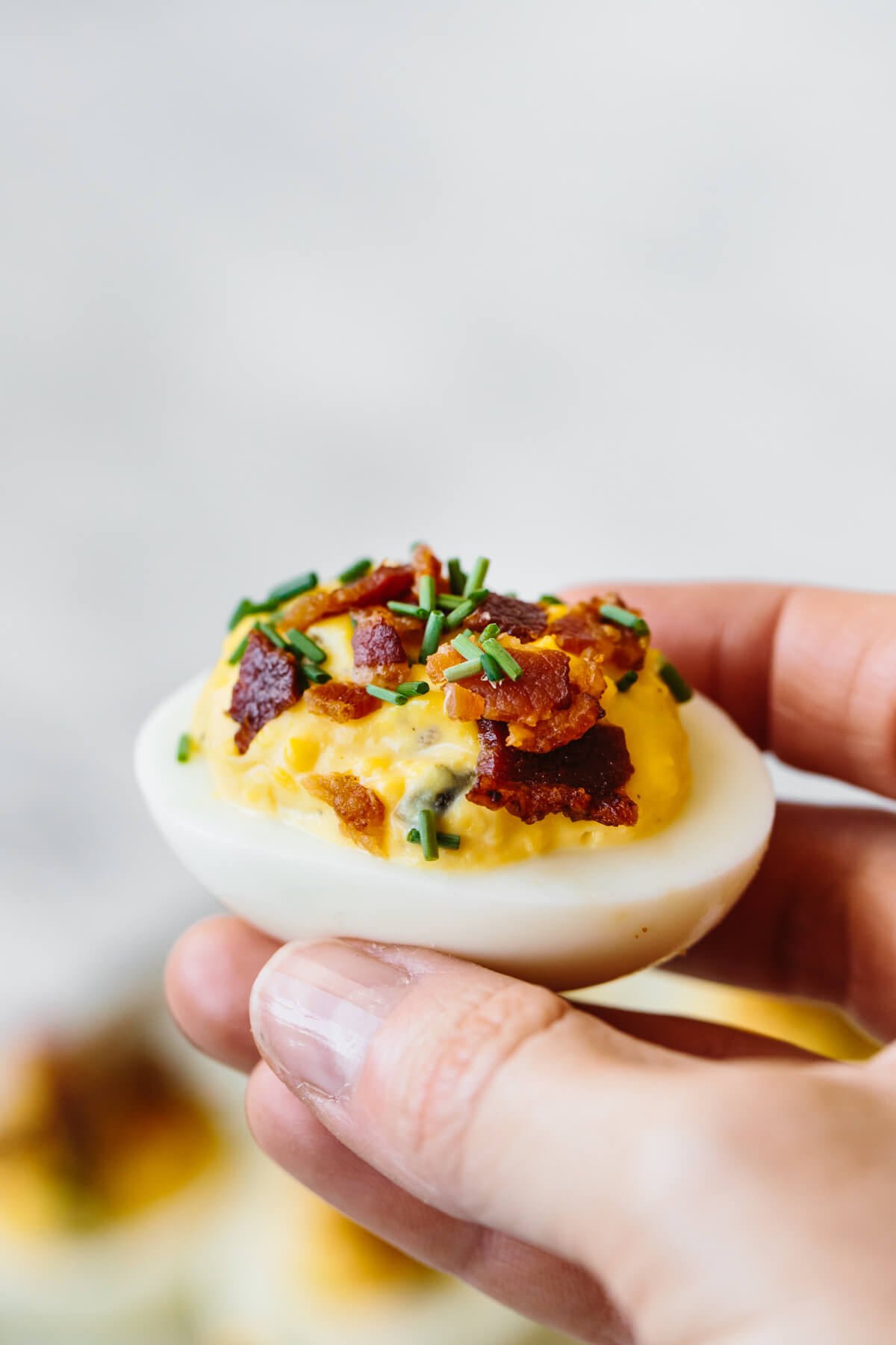 A deviled egg with bacon held in a hand, about to be eaten.