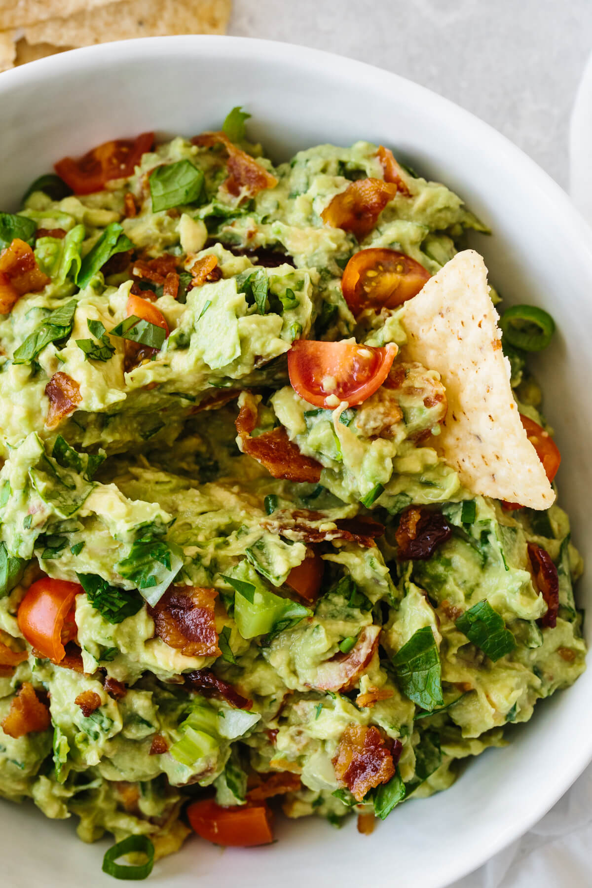 A tortilla chip taking a scoop of BLT guacamole.