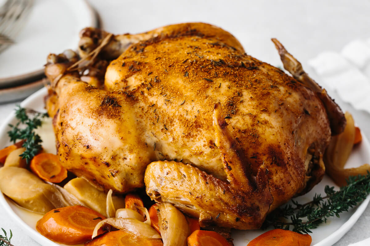 Slow cooker rotisserie chicken on a plate with vegetables.