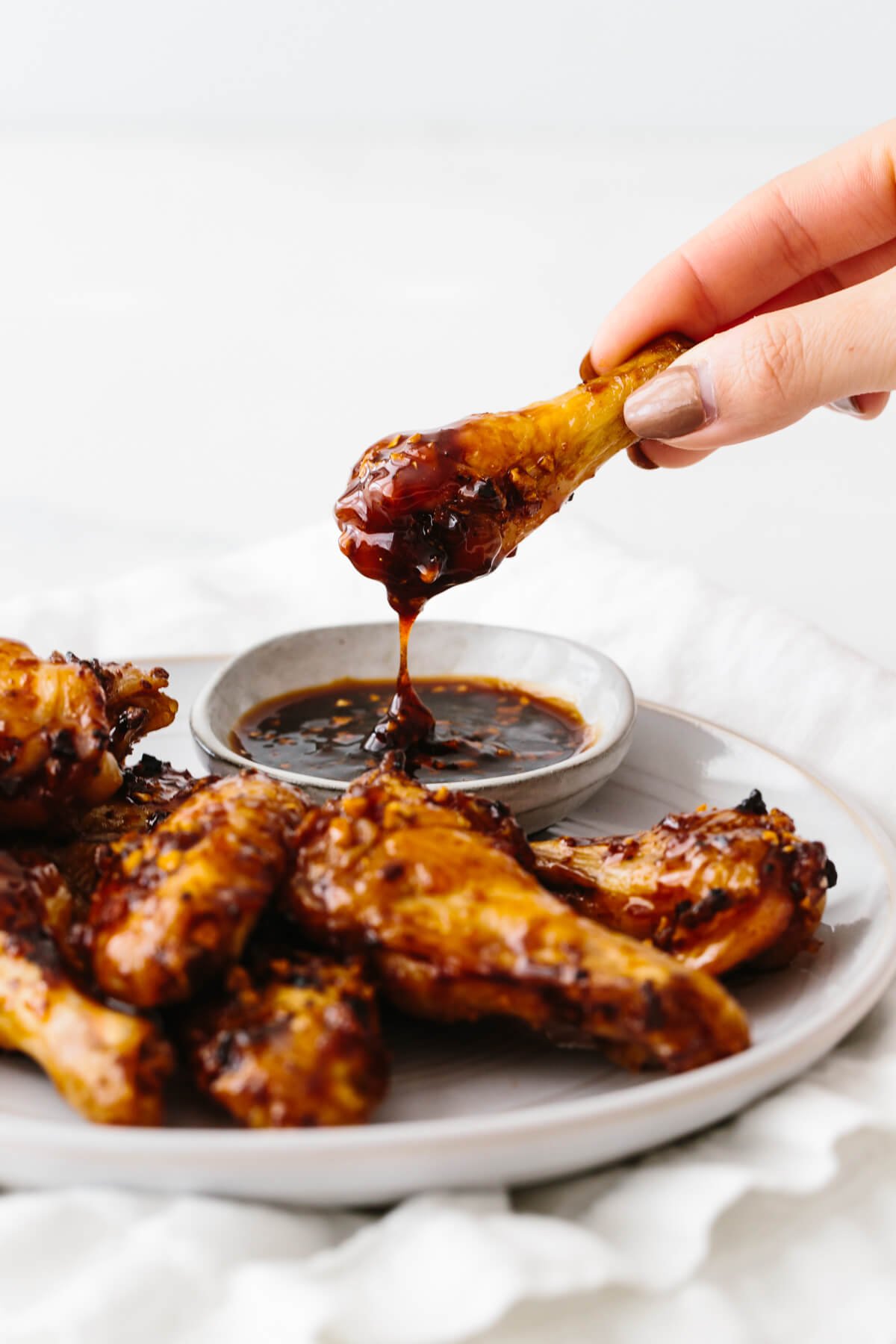 Soy garlic ginger chicken wings are a sticky, sweet and flavorful appetizer with a kick! The perfect party or Super Bowl recipe! A chicken wing dipping in soy garlic ginger sauce.
