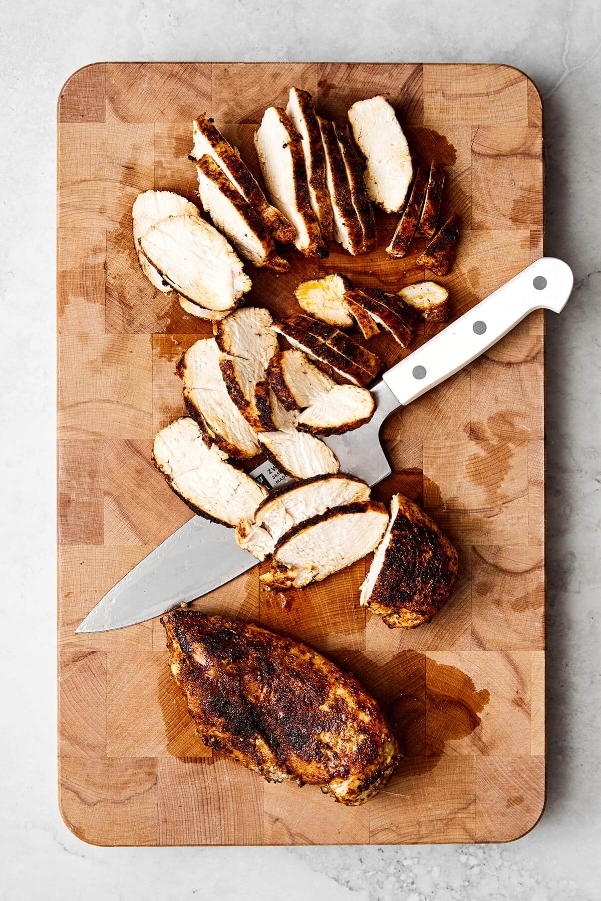Enjoy this easy skillet chicken fajitas recipe with seared chicken breast, bell peppers, and onions tossed in the best fajita seasoning. Wrap them in tortillas for taco night! Sliced chicken breast on a wooden board.