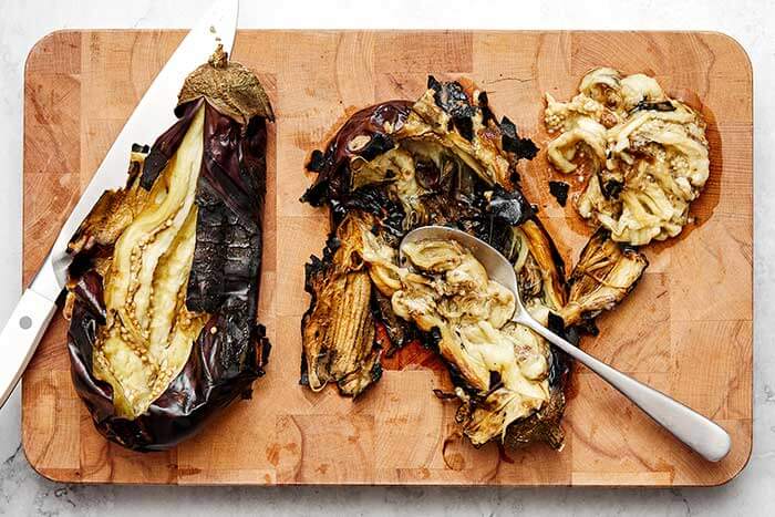 Scooping eggplant flesh with a spoon.