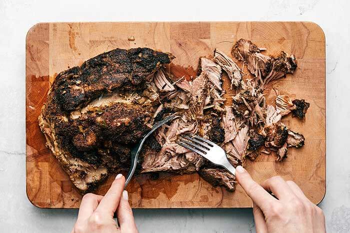 shredding carnitas on a wooden board.