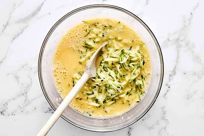 Mixing eggs with grated zucchini.