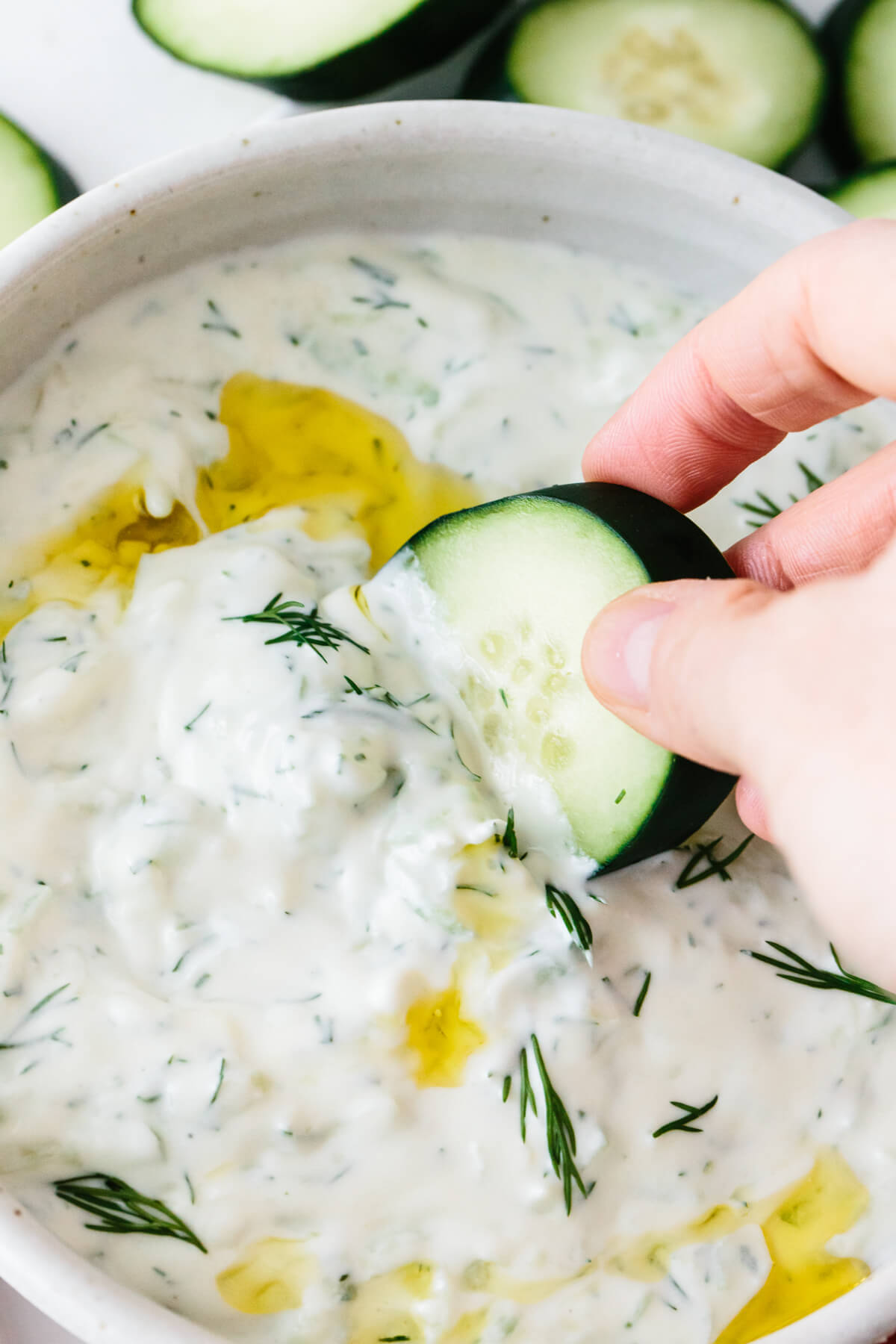 Scooping tzatziki out of the bowl with a slice of cucumber.