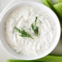 Vegan tzatziki in a bowl garnished with dill and next to pieces of celery.