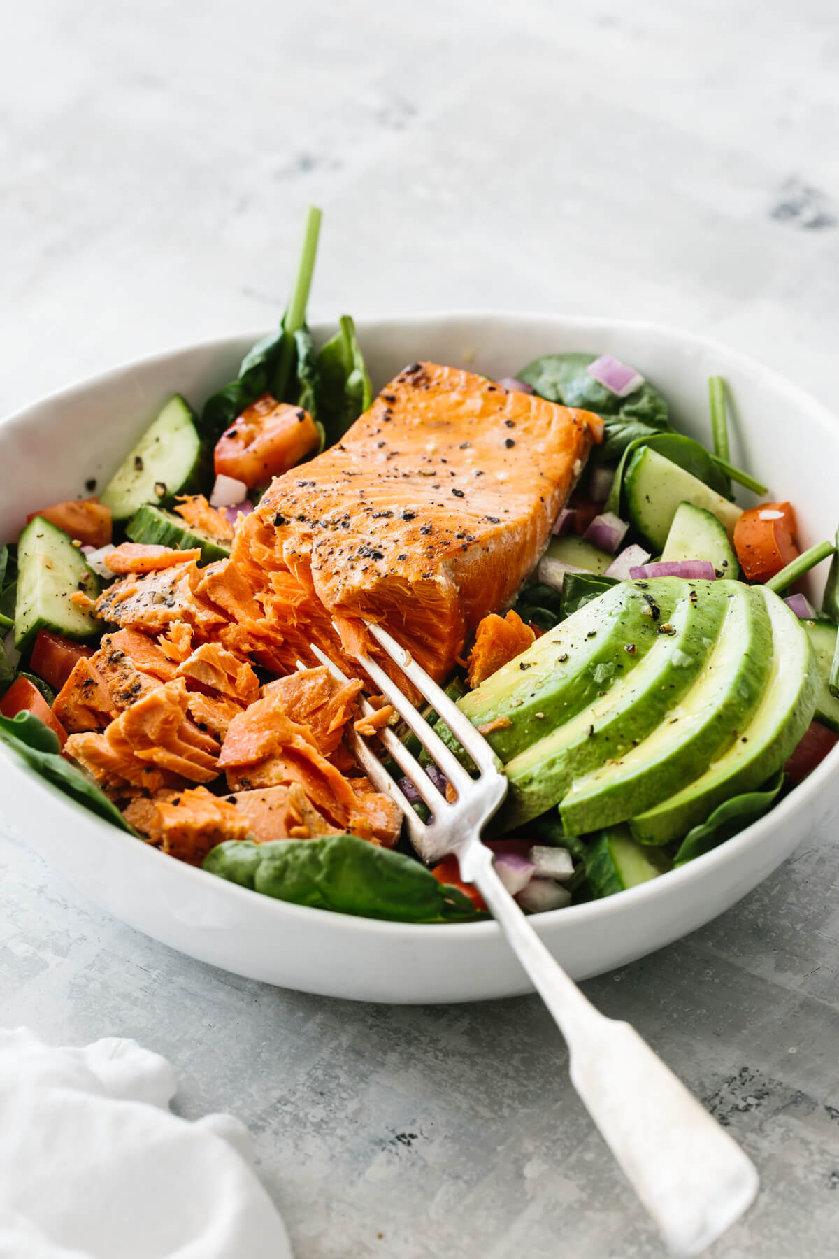 Salmon fillet broken up with fork on top of salad recipe.