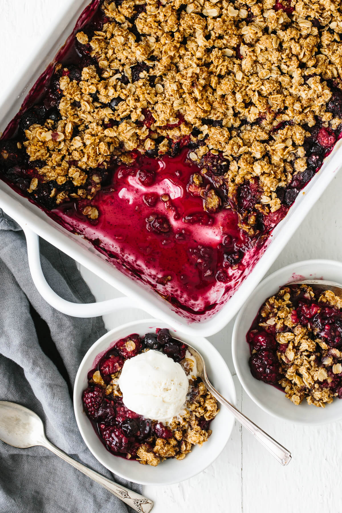 Berry crisp in baking dish with two bowls of dessert scooped out.