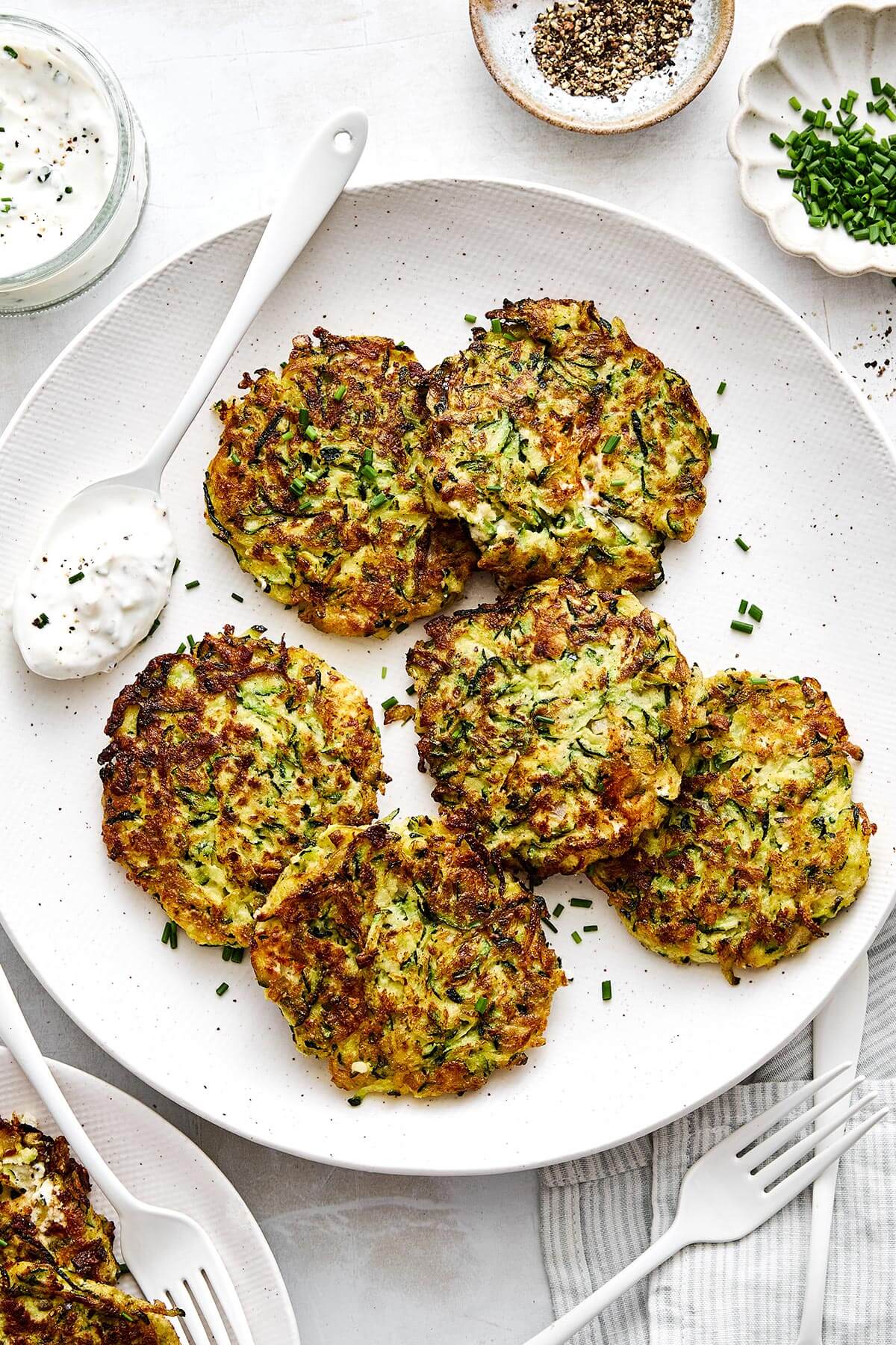 Zucchini fritters are everyone’s favorite summer dinner. With savory flavors, crispy edges, and a dollop of creamy garlic chive yogurt sauce, it's the perfect zucchini recipe to keep in rotation! Zucchini fritters on a plate.