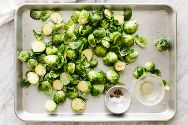 Brussels sprouts being tossed on a sheet pan with seasonings.