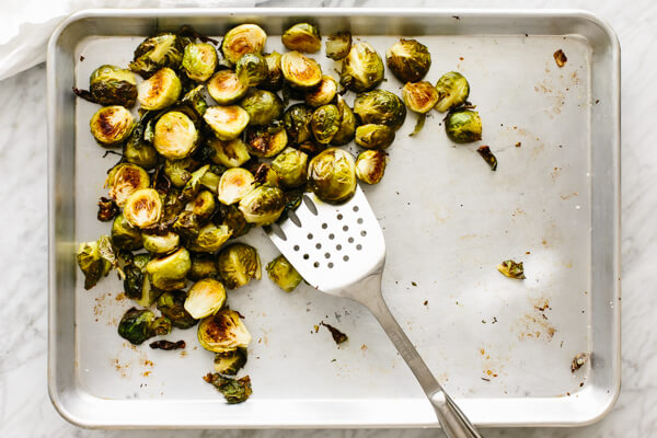 Roasted Brussels sprouts being removed from the sheet pan with a spatula.