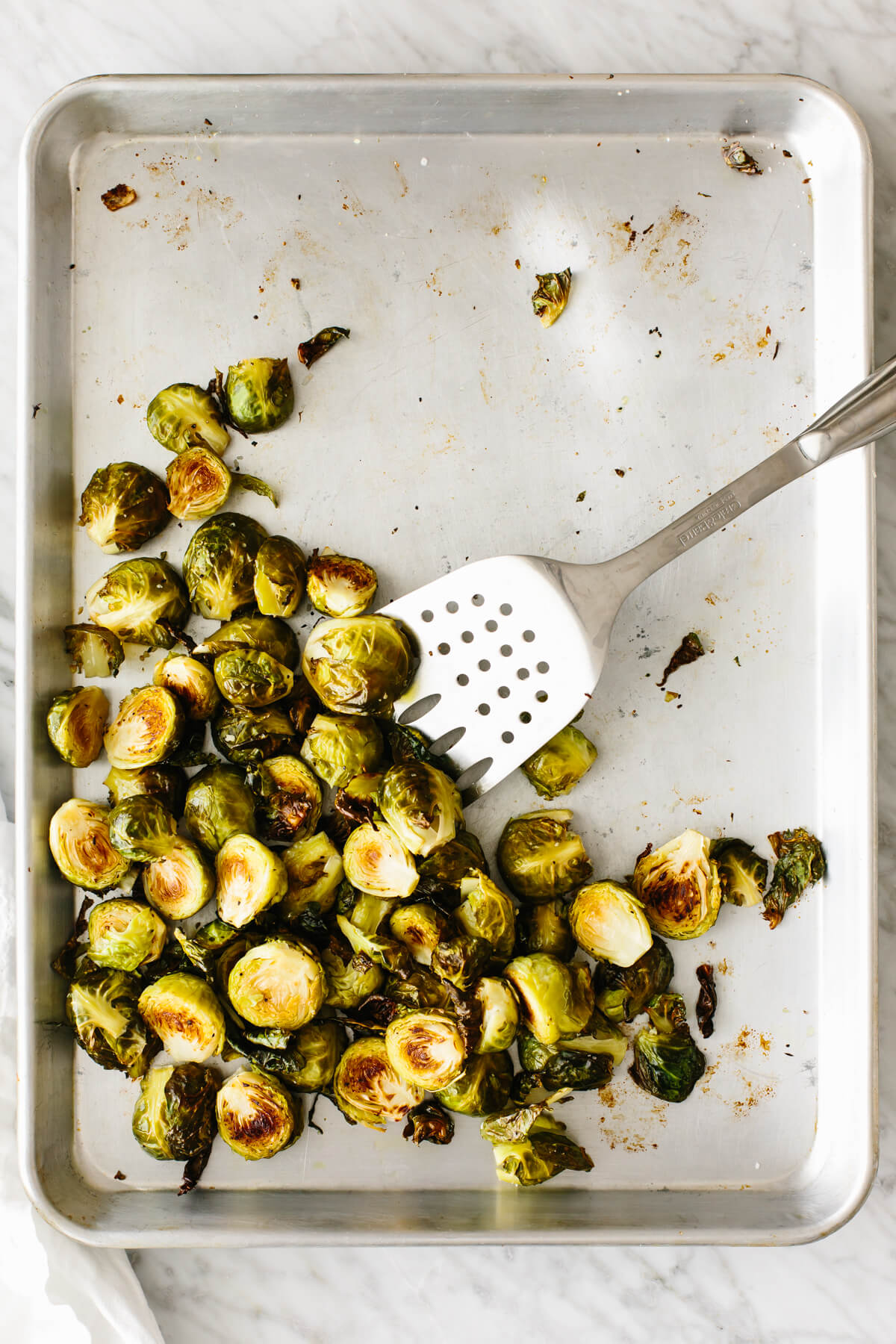Roasted Brussels sprouts on a sheet pan with a spatula.