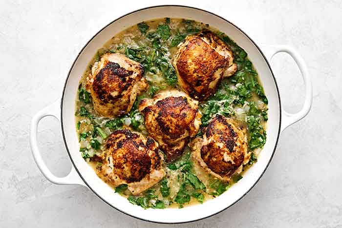 Simmering chicken thighs in an herby rice mixture in a pan.