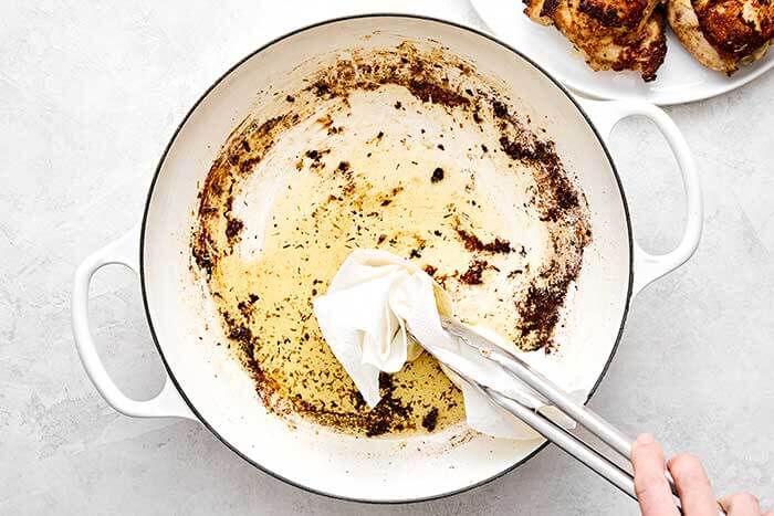Wiping off the oil in a pan with a paper towel.