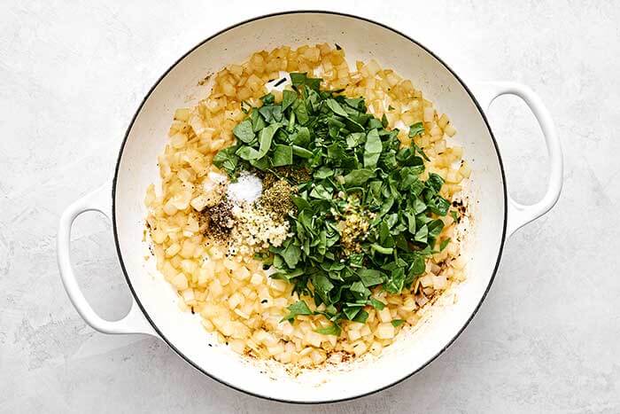 Cooking onions with herbs in a pan.
