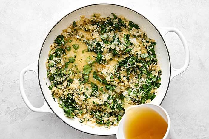 Adding rice and broth to a pan.