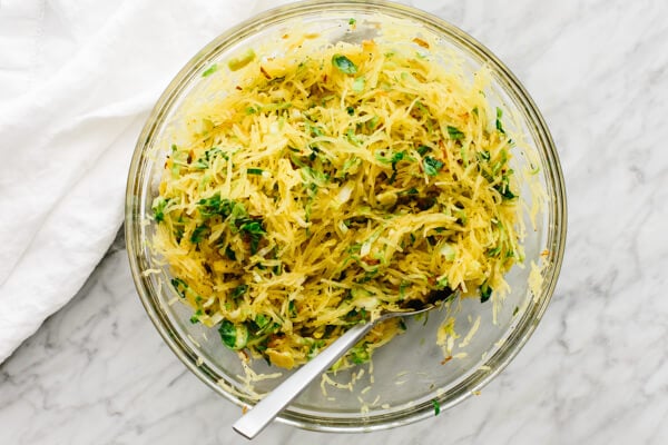 Spaghetti Squash, Brussels sprouts, and crispy shallots being mixed in a bowl.