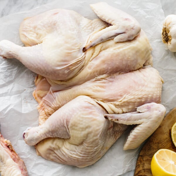 A spatchcock chicken flat on a countertop next to lemons and garlic.