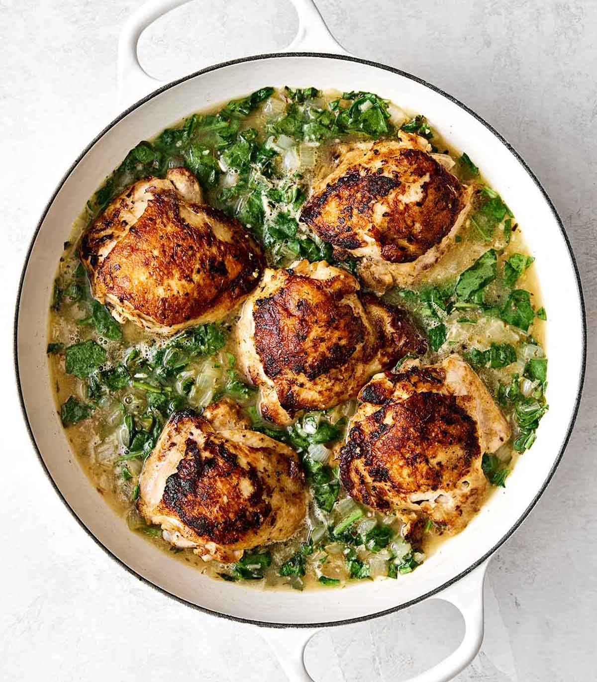 Simmering chicken thighs in an herby rice mixture in a pan.