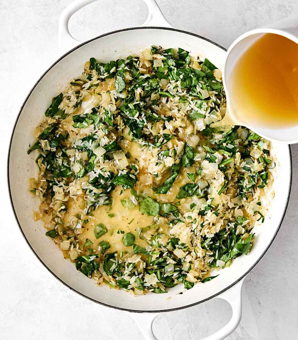 Adding broth and rice to a pan.